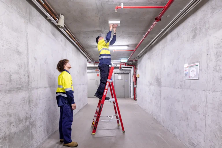 Workers installing ceiling fixture in industrial hallway