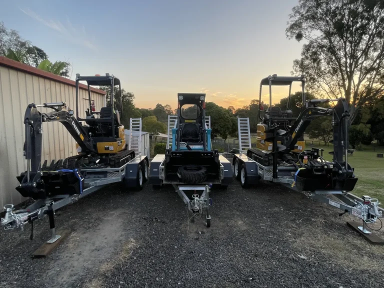 Three excavators on trailers at sunset