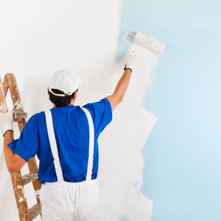 Painter applying white paint to blue wall.
