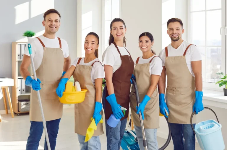 Team of smiling cleaners with cleaning supplies indoors.