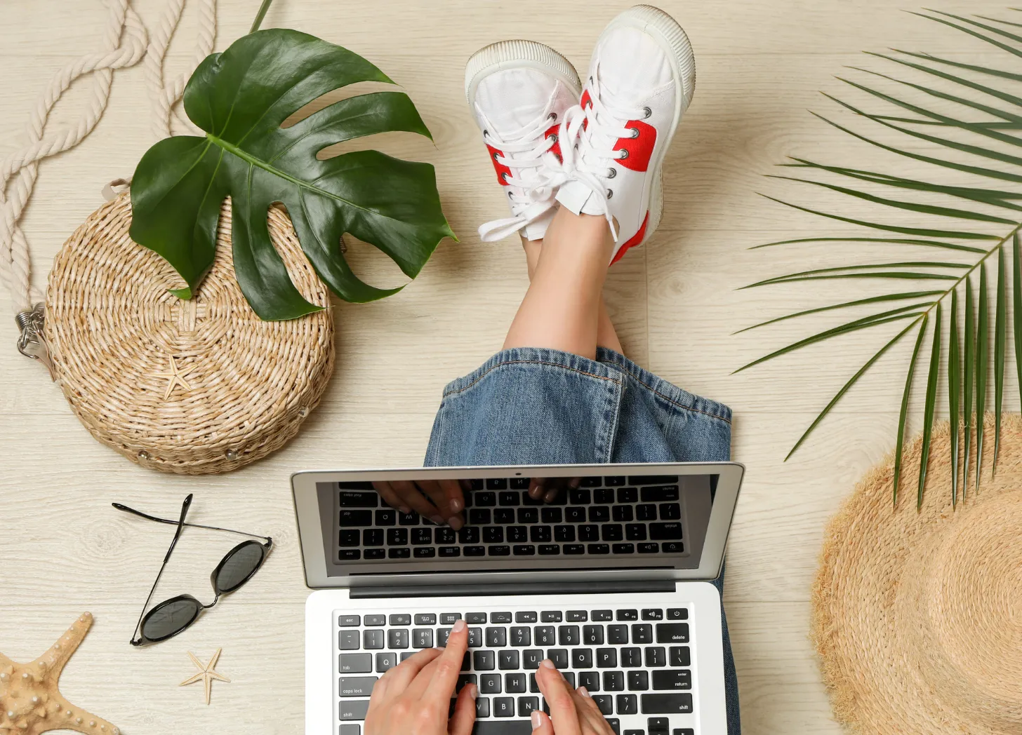 Person typing on laptop, summer beach accessories nearby.