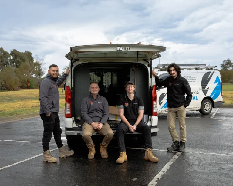Four electricians with work van in parking lot.
