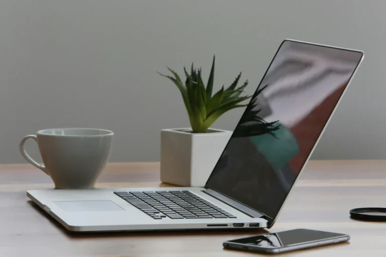 Laptop, phone, mug, and plant on wooden desk